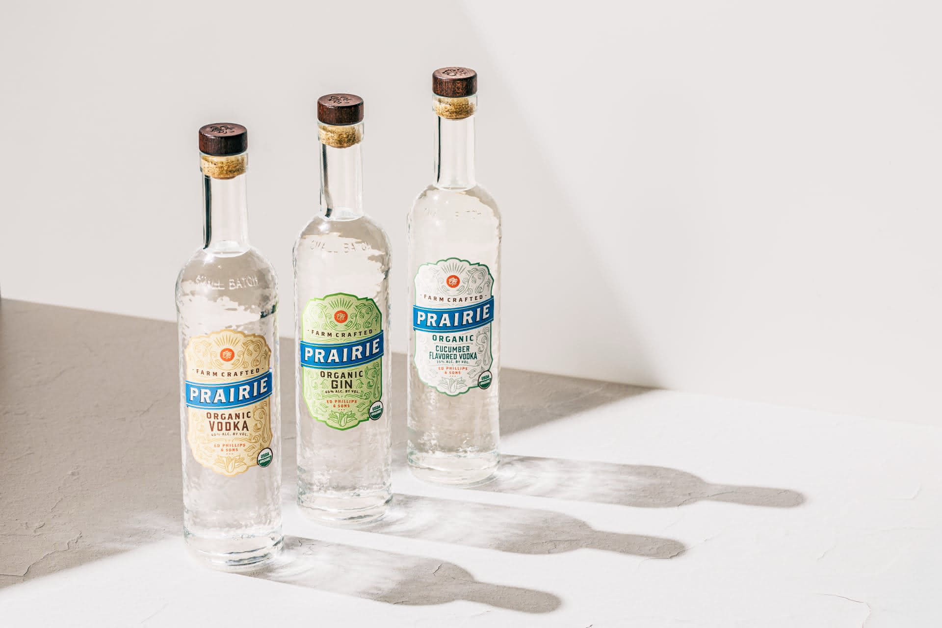 Three Prairie Organic spirit bottles — Vodka, Gin, and Cucumber Vodka — on a concrete surface with dramatic shadows