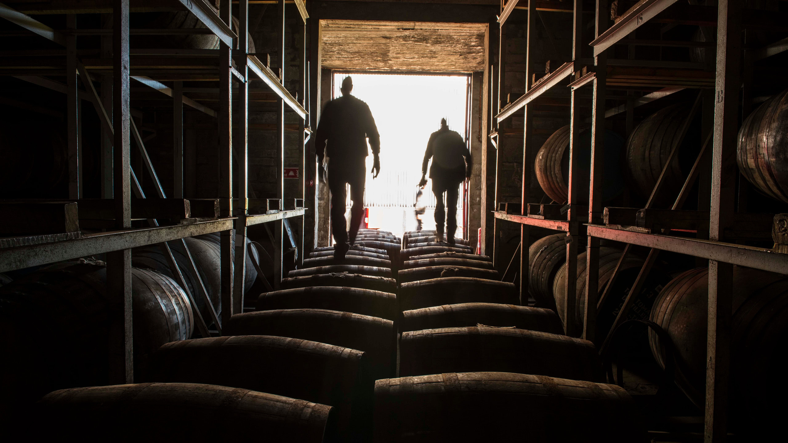Two people walking on top of a line of whisky barrels